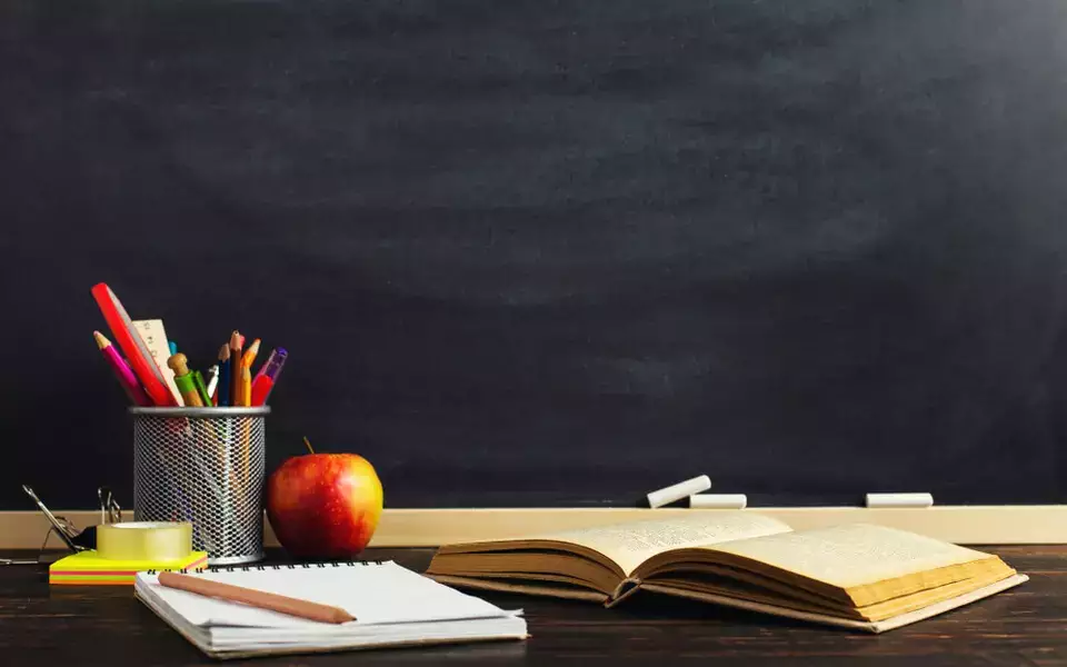 Foto com uma maça, um livro aberto e materiais escolares
